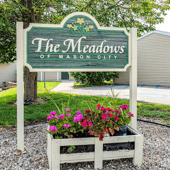 a sign that says "the meadows of mason city" with flowers in a planter box.