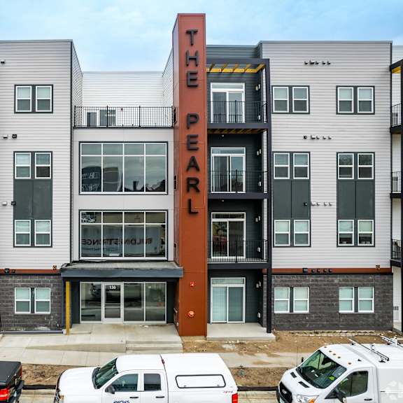 the pearl apartment building with cars parked in front.