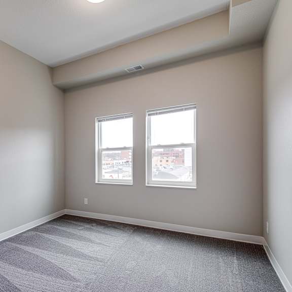 a room with a carpeted floor and two windows.