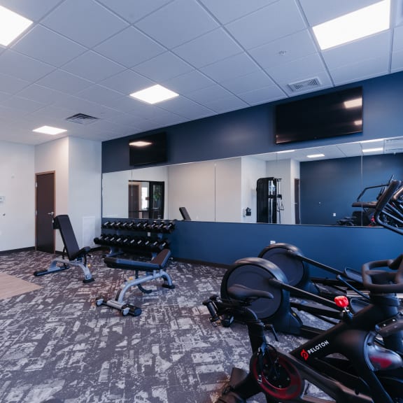a workout room with bikes and chairs and a wall mounted tv