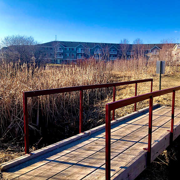 a wooden bridge with red railings leads across a body of water.