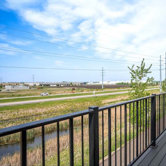 a balcony with a black railing overlooks a field with power lines in the distance.