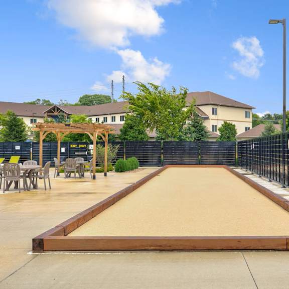 a shuffleboard court is located in a courtyard surrounded by chairs and a fence.