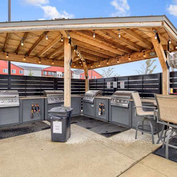 a patio with a grill and chairs under a wooden roof.
