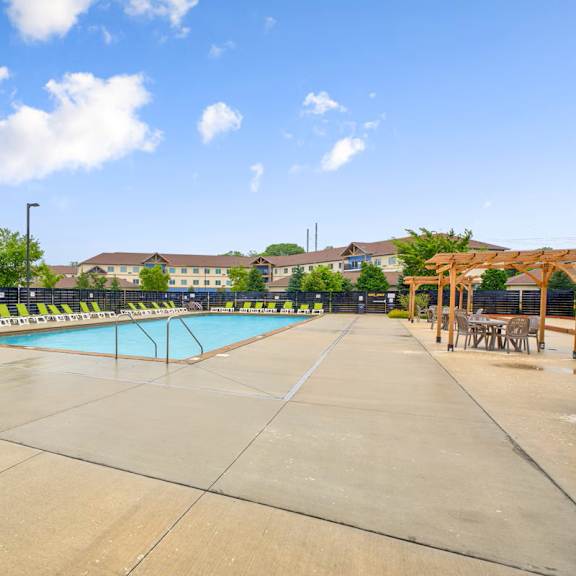 a large outdoor swimming pool surrounded by a concrete patio and lounge chairs.