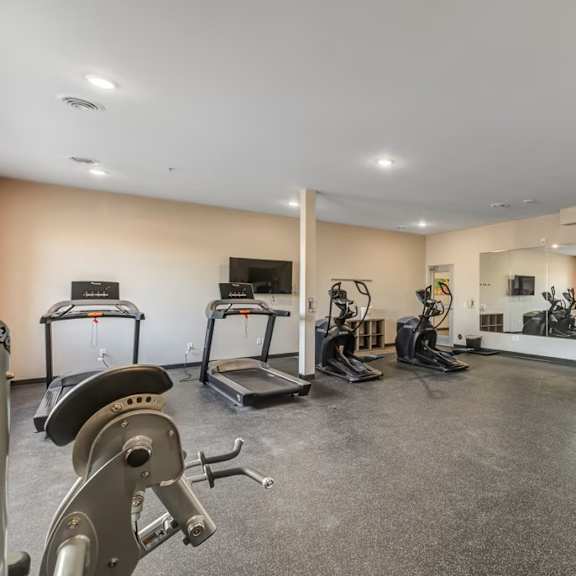 a spacious gym with a variety of equipment including treadmills, stationary bikes, and weight machines.