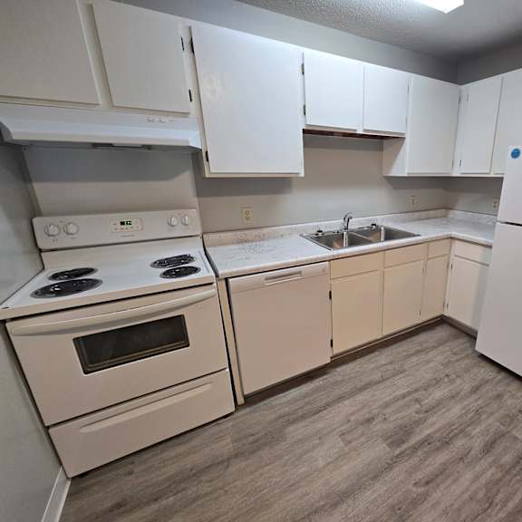 a white kitchen with a stove, oven, sink, and refrigerator.