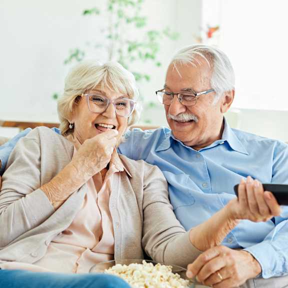 a man and a woman sitting on a couch eating popcorn and watching tv