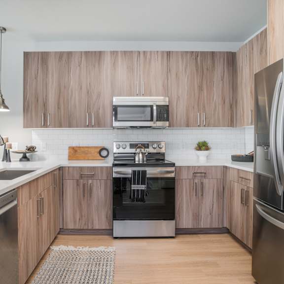 Thumbnail 1 of 9 A modern kitchen with wooden cabinets and stainless steel appliances.at The Delaney at East Park Apartments, Kennesaw, GA, 30144