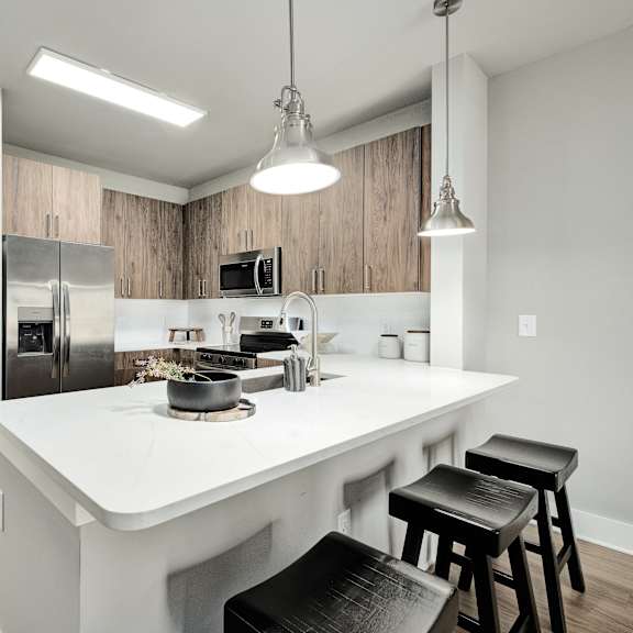 Thumbnail 3 of 13 A kitchen with a white countertop and black stools.at The Ashton at East Park Apartments, Kennesaw, Georgia
