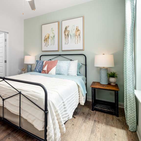 a bedroom with a black metal frame bed, a white comforter, and a small wooden table with a lamp on it.