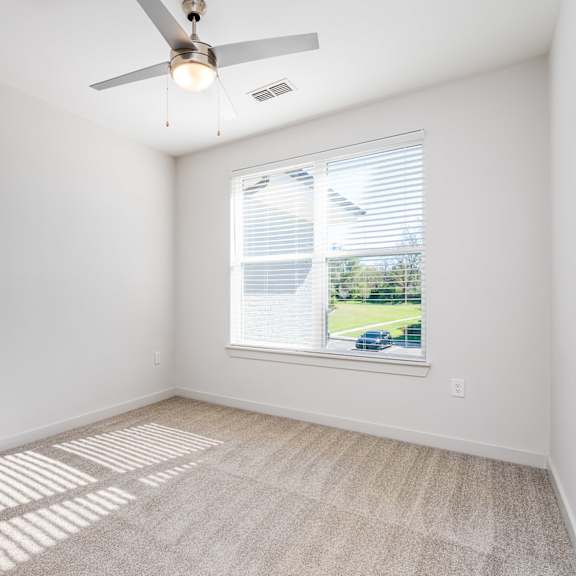 a room with a ceiling fan and a window showing a view of a house and trees outside.