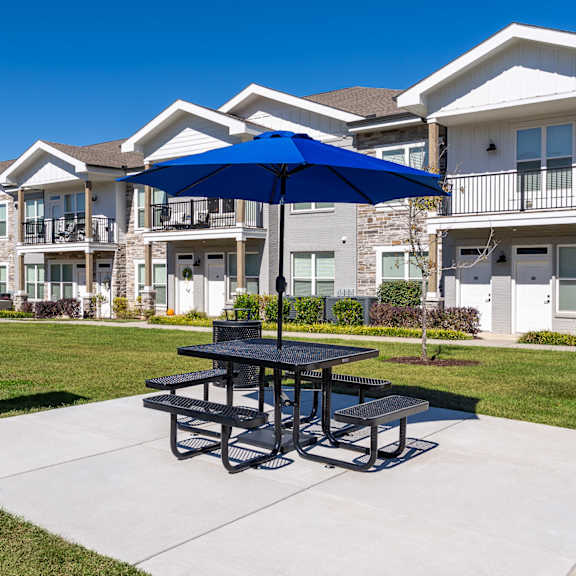 a picnic table with a blue umbrella is in the foreground of a residential area.