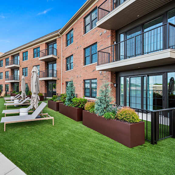 a sunny day at a modern apartment complex with a well-kept lawn and outdoor seating area.