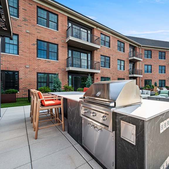 a modern outdoor kitchen setup is placed on a patio in front of a brick apartment building.