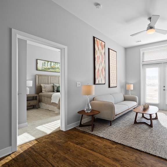 a spacious living room with hardwood-style flooring, double doors to a patio, and a ceiling fan near an doorway to a bedroom.