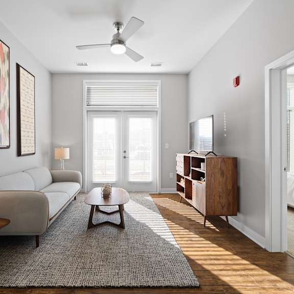 a living room with double doors to a patio providing natural light, hardwood-style flooring, a ceiling fan, and access to a bedroom.