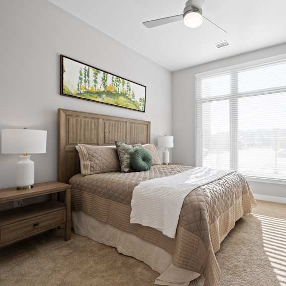 a carpeted bedroom with ample natural light from a large window and a ceiling fan.