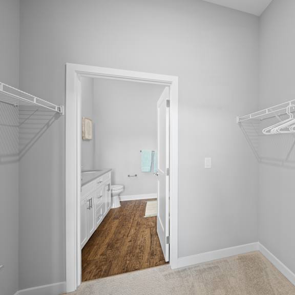 a spacious walk-in closet with clothing shelves near a doorway that leads to a private bathroom.