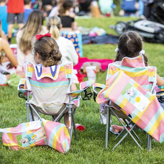 two girls sitting in chairs with colorful blankets on the grass.