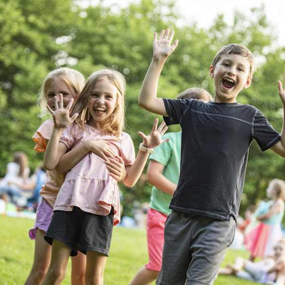 three children are playing in a park with their hands up in the air.