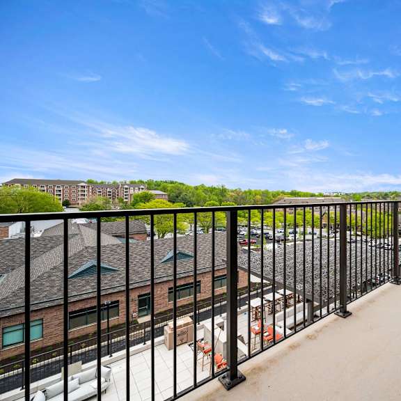 a balcony with a black railing overlooks a parking lot and buildings.
