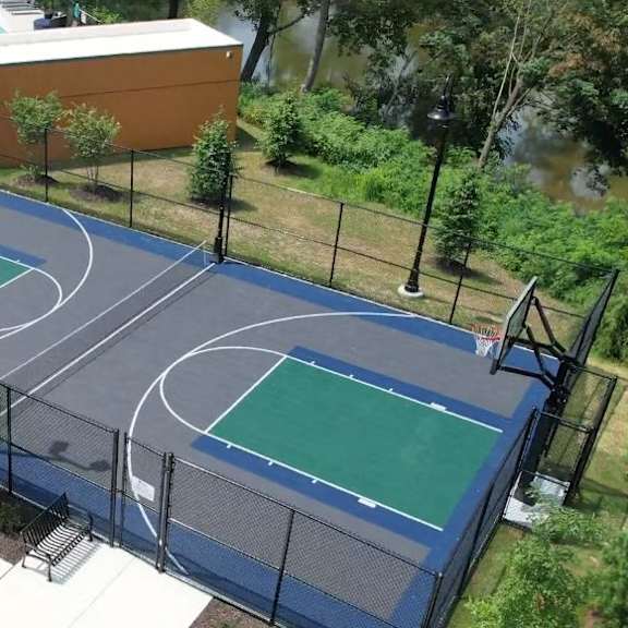 an outdoor basketball court near a gated pool and a river with trees.