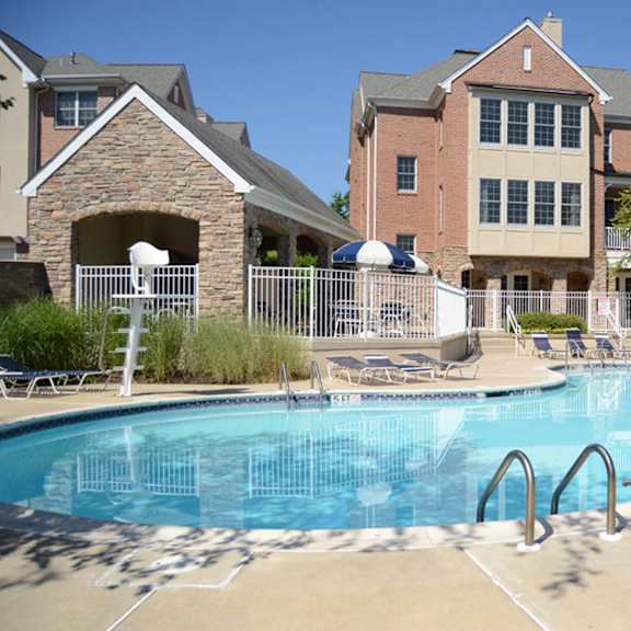 a swimming pool surrounded by chairs and umbrellas in front of a building.