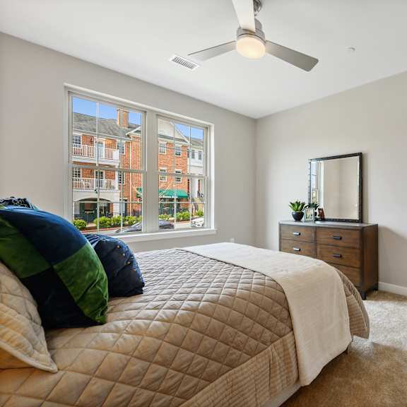 a bedroom with a large bed, a ceiling fan, and a view of a building outside the window.