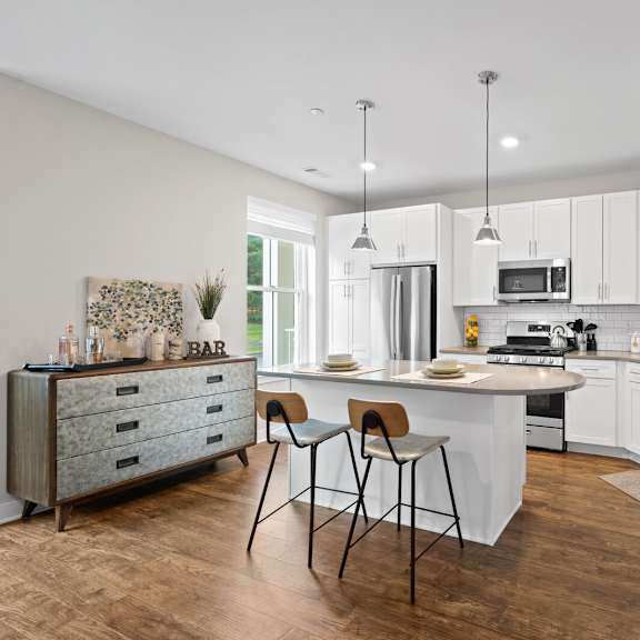 modern kitchen with white cabinetry, a white island, and two stools at hamilton at eagleview in exton, pa