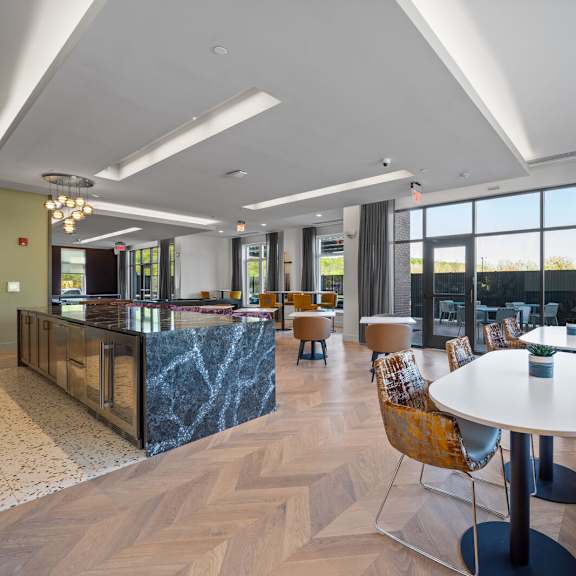 a community kitchen and resident lounge with a long bar, tables, chairs, and large windows.