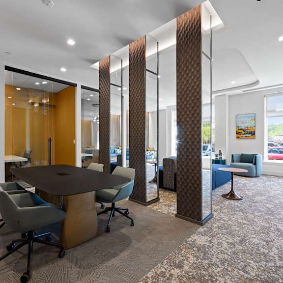 meeting rooms with tables and chairs near a community lounge with comfortable seating and large windows.