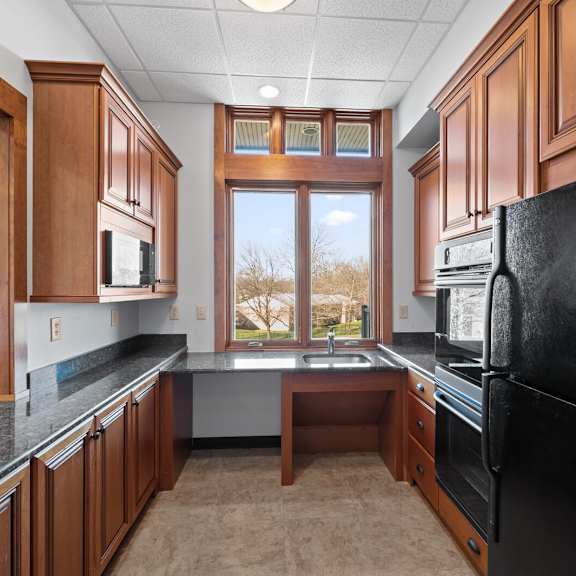 a community kitchen in the clubhouse at new kent apartments in west chester, pa, featuring a large window, black appliances, a sink, and granite countertops