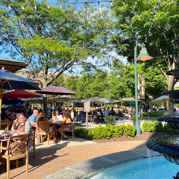a fountain in the middle of a plaza with people sitting at tables.