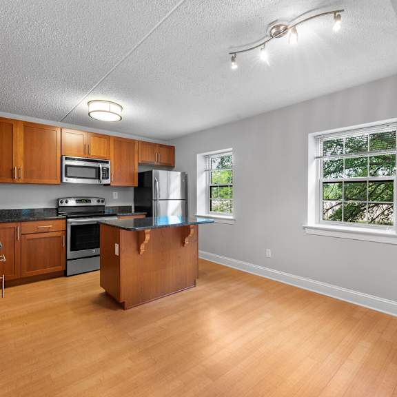 bright and spacious kitchen featuring stainless steel appliances, a central kitchen island, two windows for natural light, and hardwood-style flooring at new kent apartments, west chester, pa