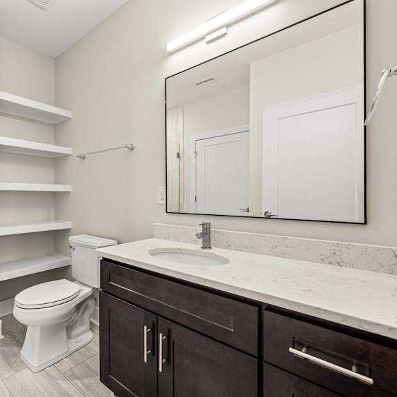 a bathroom with a toilet, sink, and shelves.