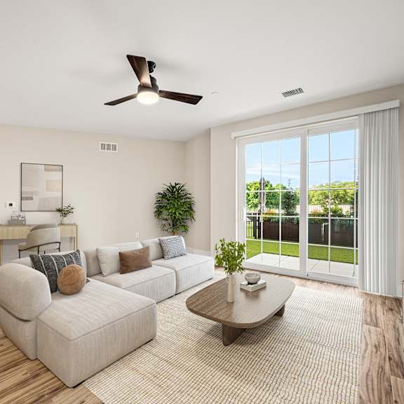 a living room with a sofa, a coffee table, a dining table, and a ceiling fan.