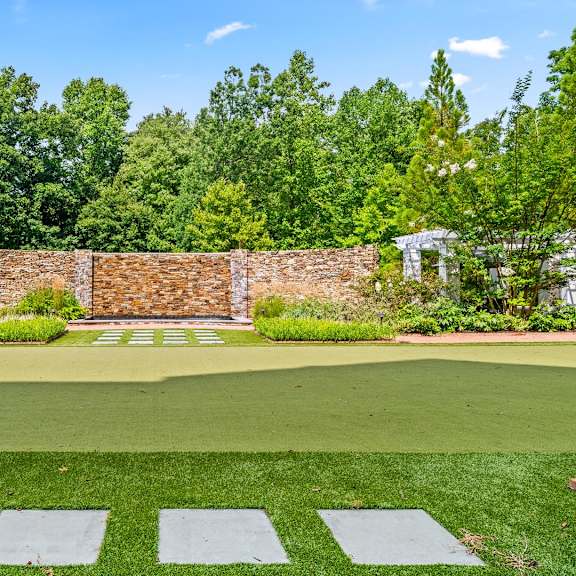 a green lawn with a brick wall and trees in the background.