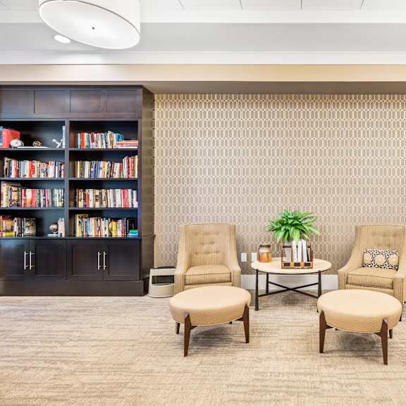 a room with a carpeted floor, two chairs, a table, and bookshelves filled with books.