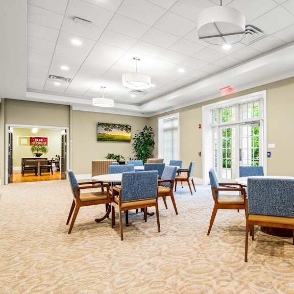 a room with a table and chairs in the foreground and a window with blinds in the background.