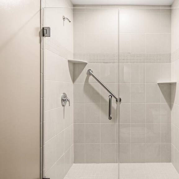 a white tiled shower with a glass door and a metal grab bar.