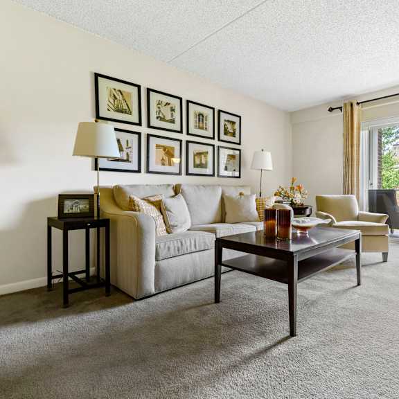 a spacious living room at new kent apartments in west chester, pa, featuring carpet flooring, sliding doors leading to a private balcony, and plenty of natural light