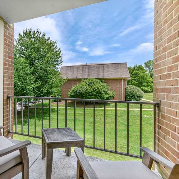 a covered balcony with two chairs, a small table, and two doors leading to a storage closet in an aspen floor plan at new kent apartments, west chester, pa