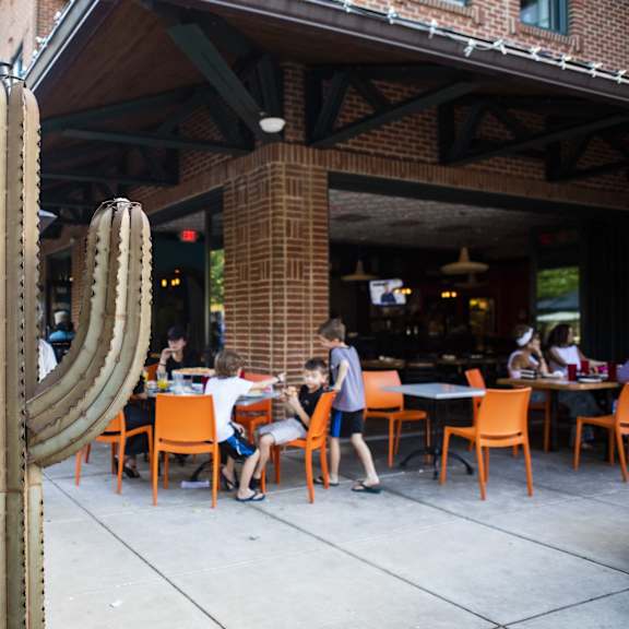 a cactus stands in front of a restaurant with people sitting at tables.