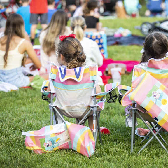 two girls sitting in chairs with colorful blankets on the grass.