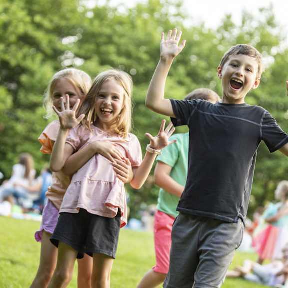 three children are playing in a park with their hands up in the air.