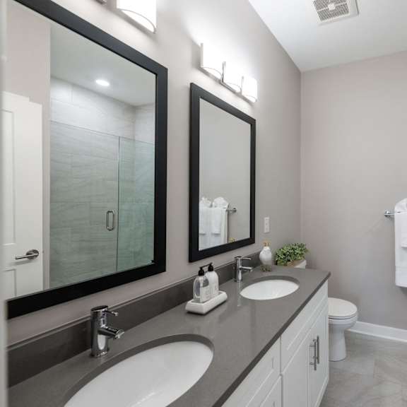 luxury apartment bathroom featuring quartz countertops, a dual-vanity setup, frameless glass shower doors, and an oversized soaking tub at claremont on the square in exton.