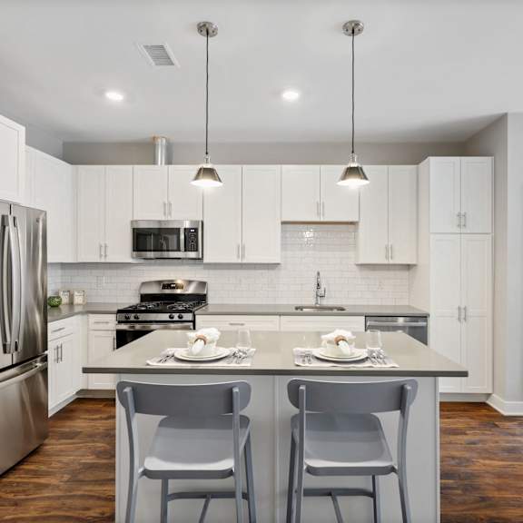 modern luxury apartment kitchen featuring an oversized island, stainless steel appliances, gas range, quartz countertops, and light contemporary finishes at claremont on the square in exton.