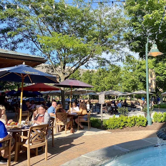 a fountain in the middle of a plaza with people sitting at tables.