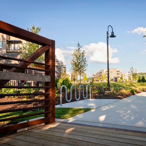 a large green space with a walking trail, path lights, trees, bike station, and bridge near river station apartment buildings.